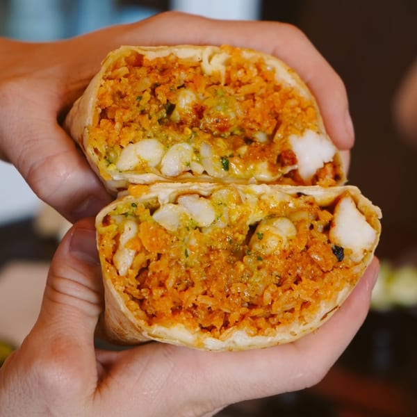 Hands holding a Flying Burro burrito, cut in half, revealing rice, beans, and white cheese.