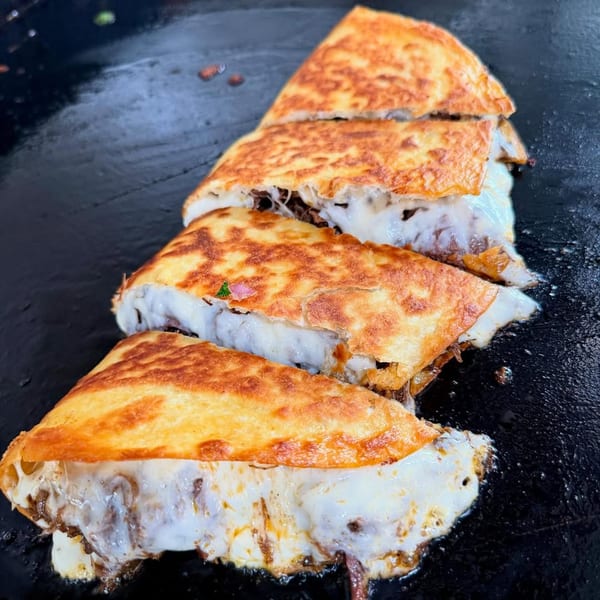 Four cheesy quesadillas with meat filling, cooking on a dark, flat griddle at Flying Burro.