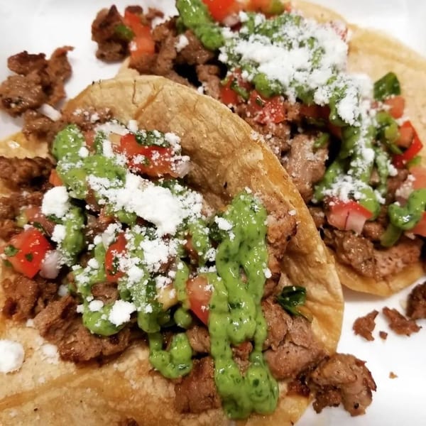 Two Flying Burro tacos with meat, salsa, green sauce, and cotija cheese.